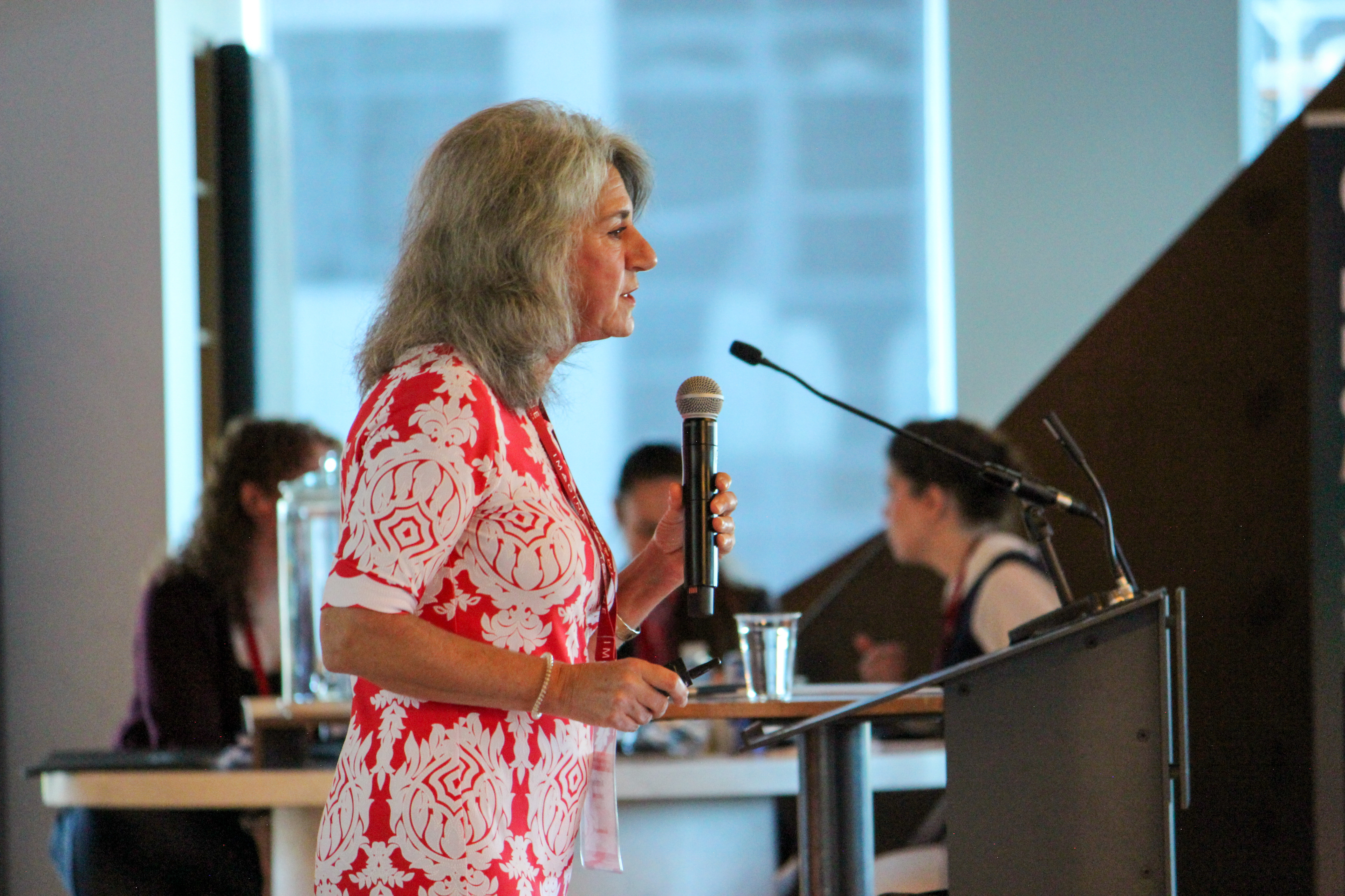 Armine Yalnizyan parle dans un micro à un podium lors d’un événement en intérieur.