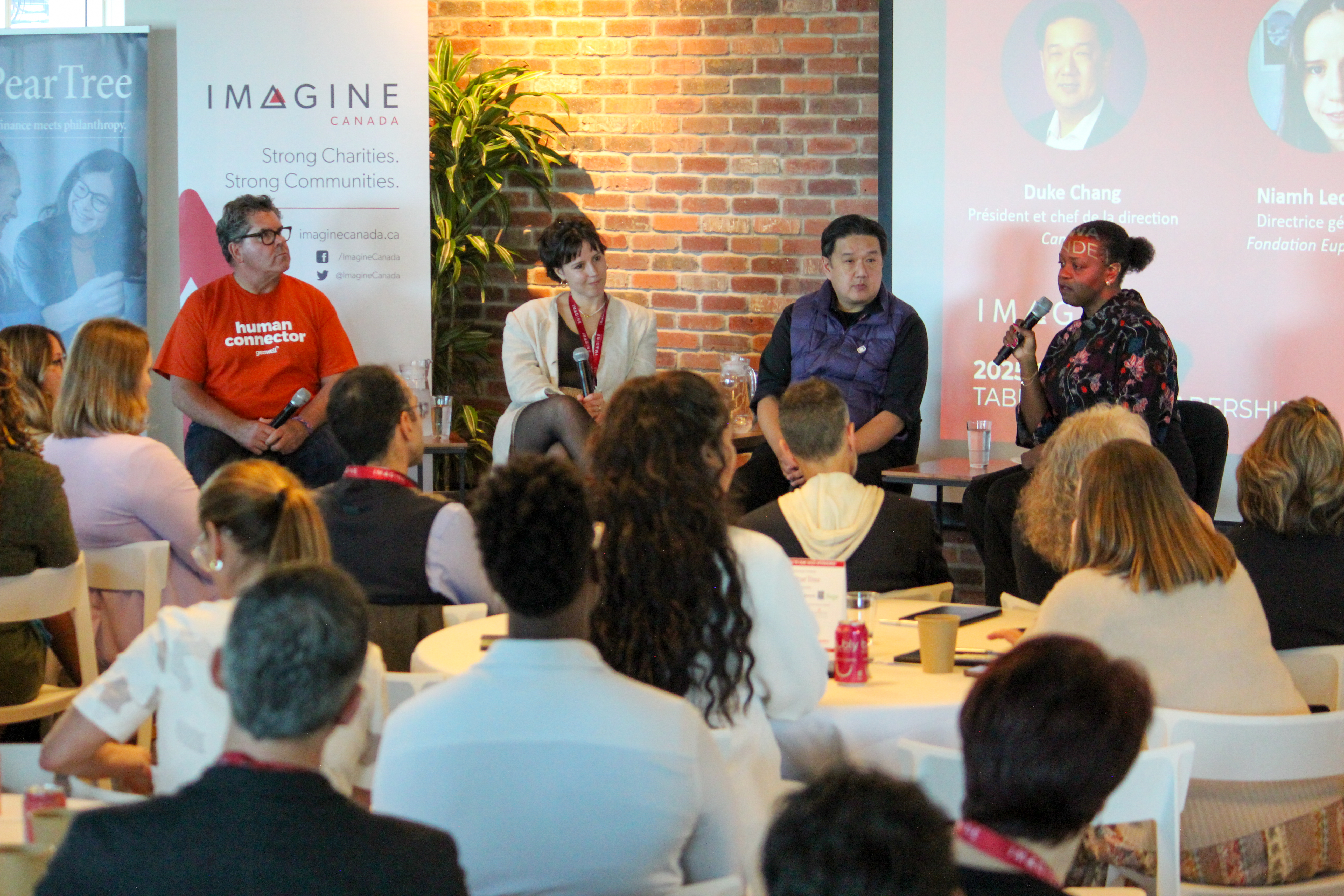 Quatre panélistes s’adressent à un public assis lors d’un événement Imagine Canada, avec écran projeté et banderoles promotionnelles en arrière-plan.