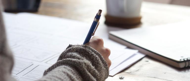 hand holding pen with notebook and mug on table