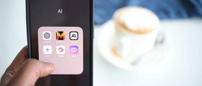 Une personne tient un smartphone affichant un dossier IA avec diverses icônes d'applications, notamment ChatGPT, Midjourney, Claude, Gemini, CoPilot et Poe.