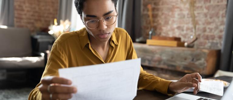 Focused woman in eyeglasses looking through paper documents