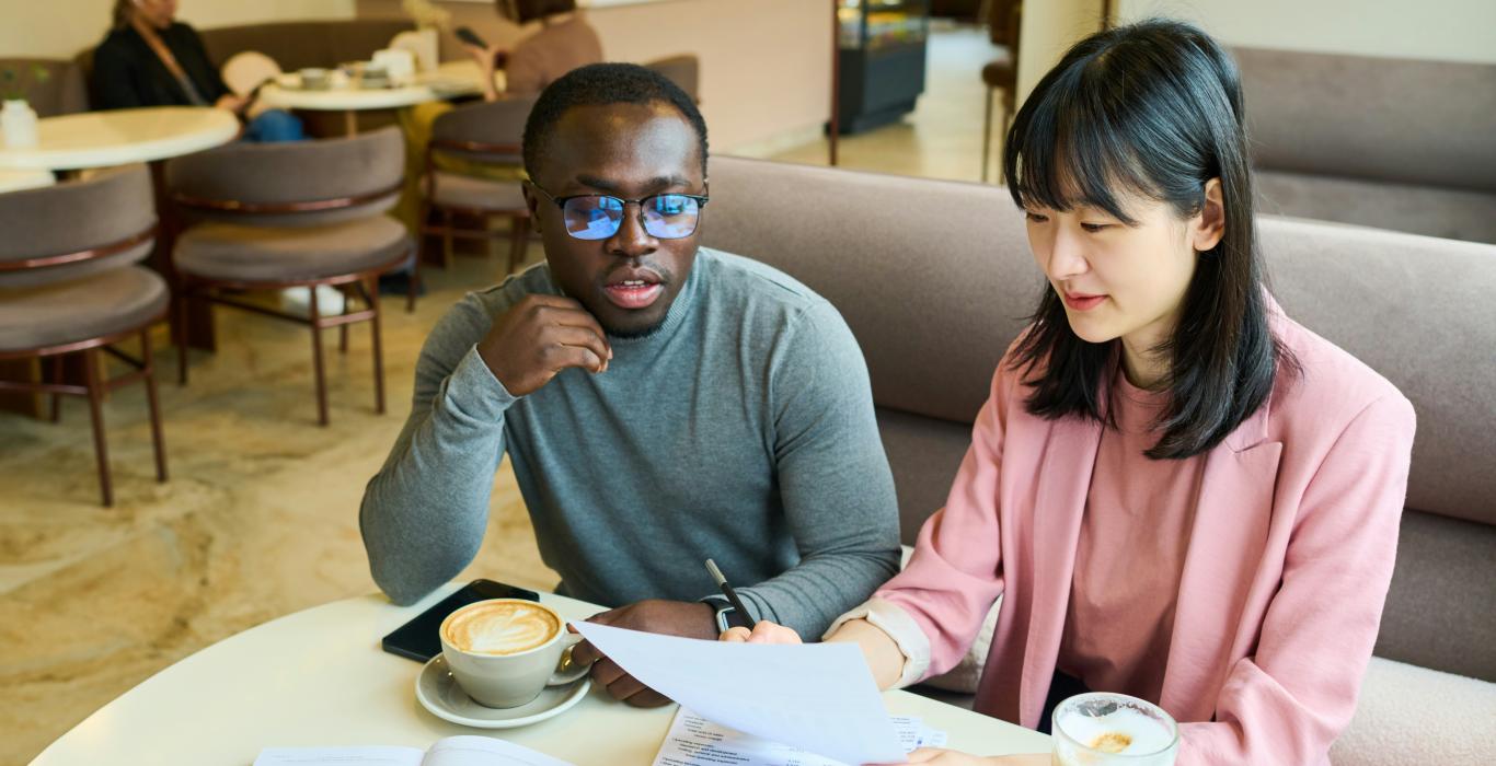 Deux professionnels se rencontrent dans un café et examinent ensemble des documents imprimés autour d'un café.