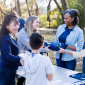 Un groupe de bénévoles souriants distribue des t-shirts bleus et des badges lors d'un événement communautaire en plein air.