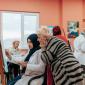 Woman painting on a canvas while an older woman observes during a group art workshop.